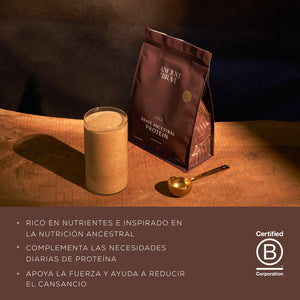 Glass of protein shake next to a bag of Brave Ancestral Protein on a wooden surface with a dark 